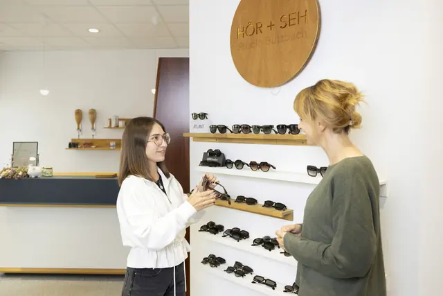 Mitarbeiterin reicht einer Kundin eine Sonnenbrille
